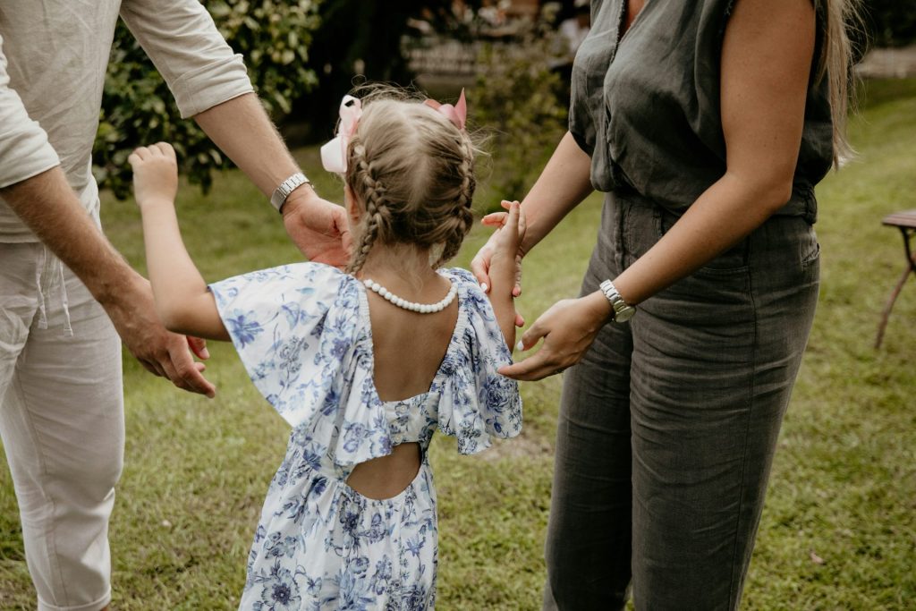 a little girl in a blue dress holding hands with her parents